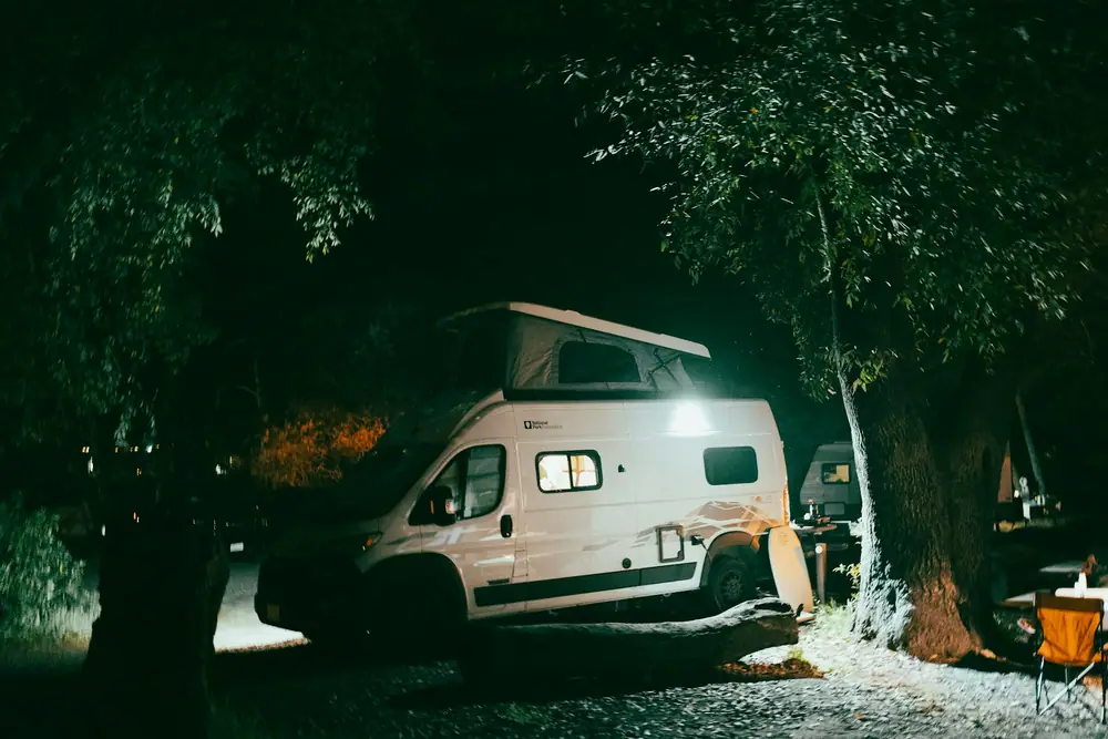 Campervan nachts auf einem bewaldeten Campingplatz mit eingeschalteter Innenbeleuchtung