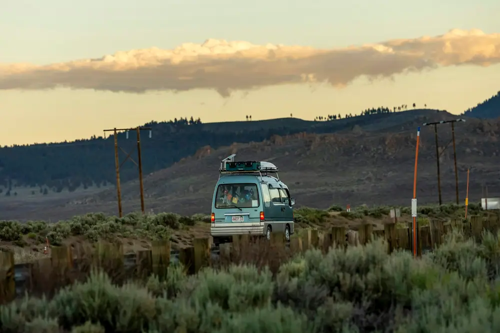 Blauer Campervan in offener Buschlandschaft mit Hügeln im Hintergrund im Abendlicht