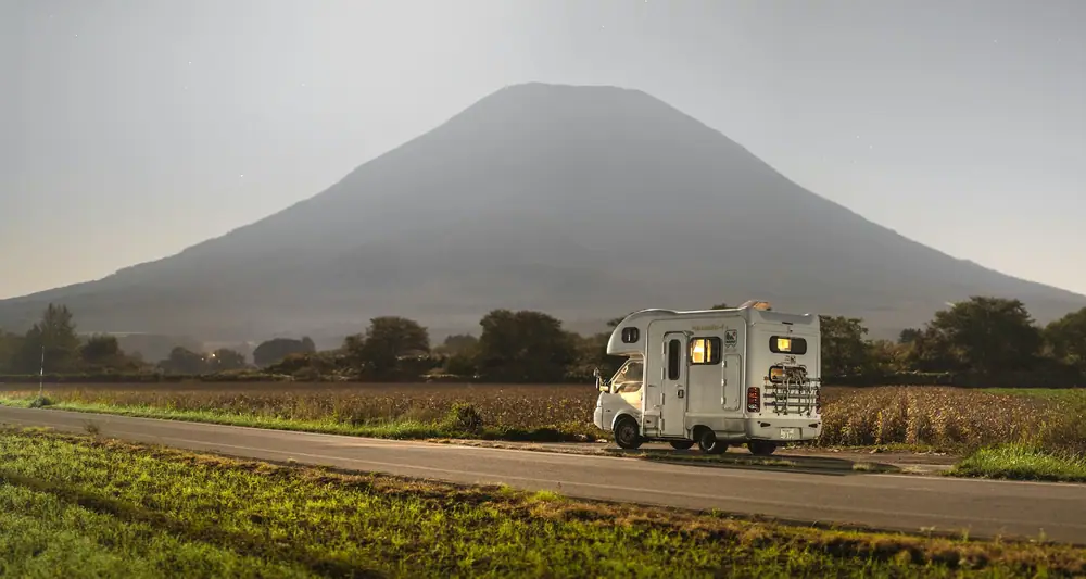 Kleines Wohnmobil auf einer geraden Straße mit einem großen Berg im Hintergrund