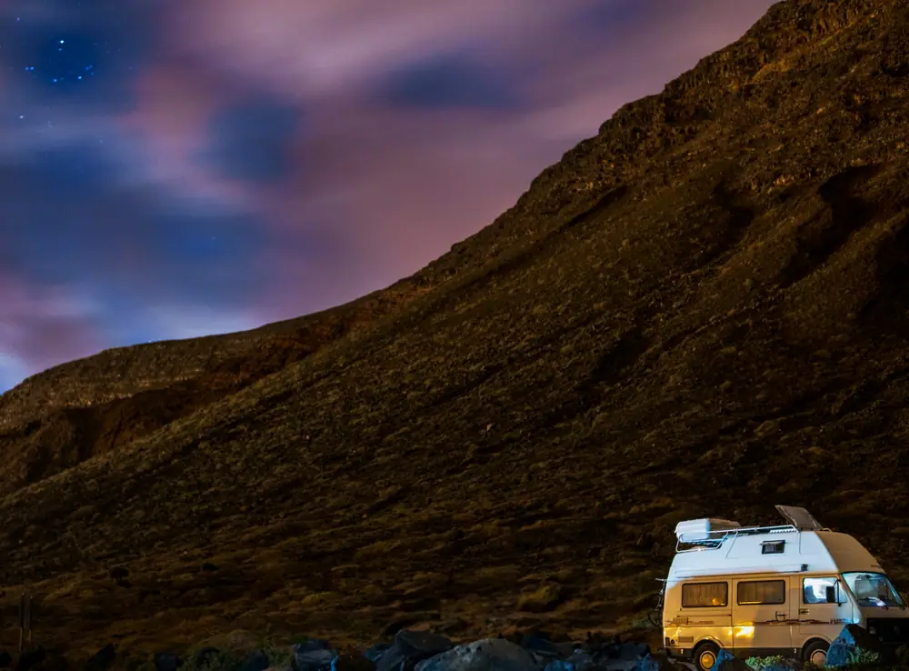 Kleiner Campervan in der Abenddämmerung unterhalb eines felsigen Berghangs